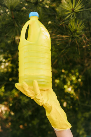 A person with yellow gloves holding a yellow plastic bottle - plastic pollution concept