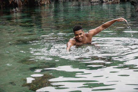 A beautiful shot of a young fit man with a cool hairstyle swimming in the lake while smilingの写真素材