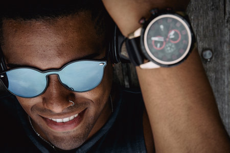 A young fit man with sunglasses working out in the park while listening to music in headphones
