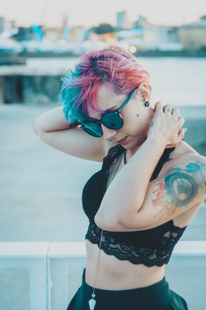 A portrait of a young female with tattoos and pink and blue hair playing with her hair posing in an amusement parkの写真素材
