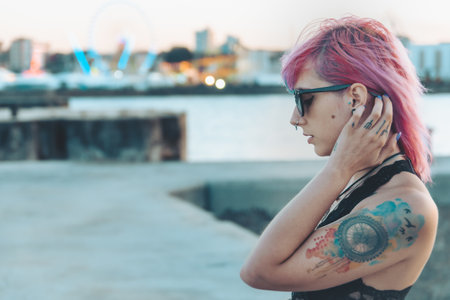 A portrait of a young female with tattoos and pink and blue hair playing with her hair posing in an amusement parkの写真素材