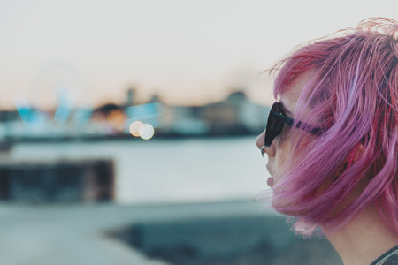 A closeup shot of a pretty pink-haired young female with a piercing and sunglassesの写真素材