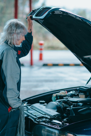 An attractive young blonde female wearing an auto mechanic uniform and repairing the car