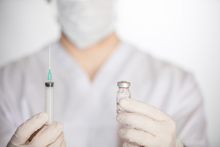 A health worker holding syringe and vial with vaccine against COVID-19, measles and fluの写真素材