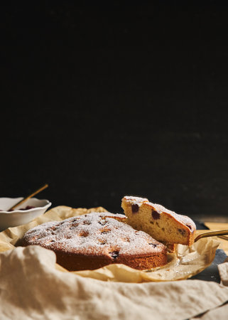 A vertical shot of a Cherry Cake with sugar powder and ingredients on the side on a black background
