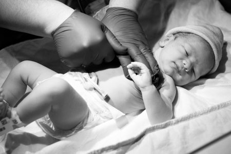 A greyscale closeup of a doctor checking a newborn child under the lights in a hospitalの写真素材