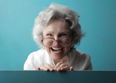 A white-haired lady with glasses and a wide smile behind a turquoise wall