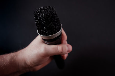 A closeup shot of a microphone in the hand of a person on a black backgroundの写真素材