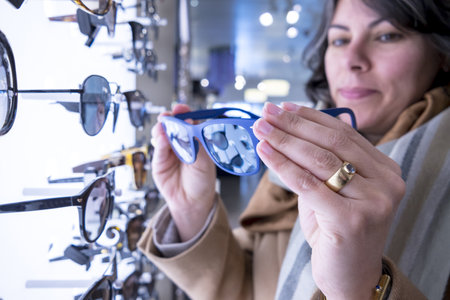 A selective focus shot of a female holding a blue sunglasses with a blurred backgroundの写真素材