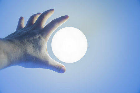 A hand reaching for a lit lamp hanging from a blue ceilingの写真素材