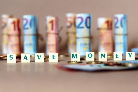 White cubes spelling Save Money on the table with Spanish Dinero bills and coins