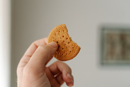 A selective focus of a person holding a bitten cookie under the lights with a blurry backgroundの写真素材