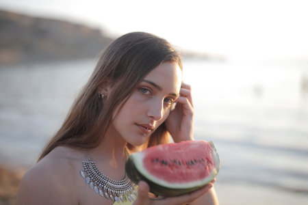 A shallow focus shot of an attractive female holding a melon while looking at the cameraの写真素材