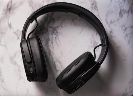 A high angle view of black wireless headphones on the table under the lights