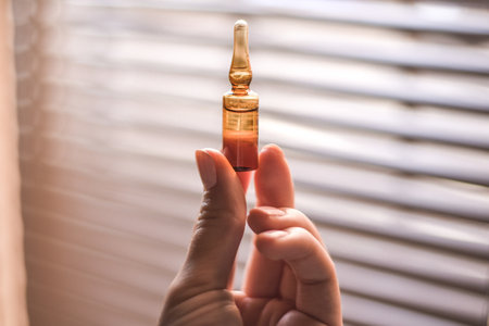 A closeup of a person holding an ampoule under the sunlight with a window on a blurry background