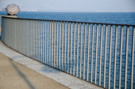 A railing on the body of the lake and a person with an umbrella in the backgroundの写真素材