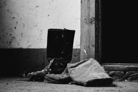 A greyscale closeup of old boots on the ground near an abandoned building - cool for backgroundsの写真素材