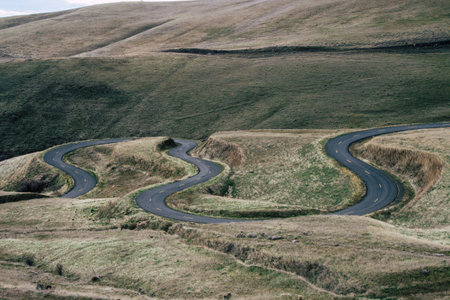 A landscape of a curvy road surrounded by hills covered in the grass at daytimeの写真素材