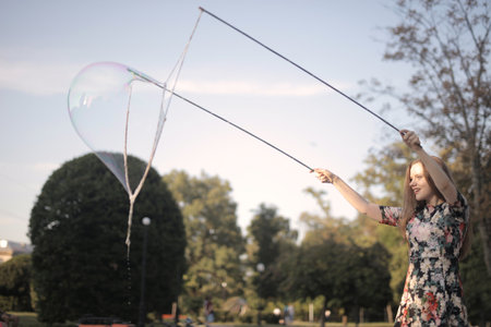 A beautiful picture of a girl making a big soap bubble in the park against a blurry background