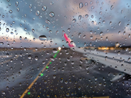 A blurry view of an airport runway through an airplane window with rain dropsの写真素材