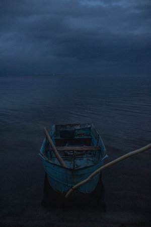 An eerie shot of a docked small blue boat in the sea on a gloomy dayの写真素材