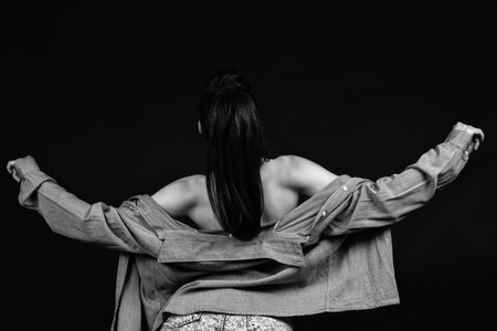 A greyscale shot of the back of a female with a jacket on and open arms under the lights in a studioの写真素材
