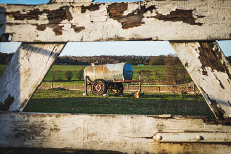 An old water truck for animals on a field edged by a wooden fence.の写真素材