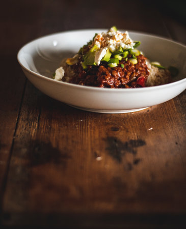 A vertical shot of a tasty dish with rice and sauce in a white plate on a wooden tableの写真素材
