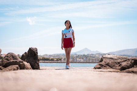 A female wearing a white shirt and a red mini skirt captured by the ocean in Spainの写真素材