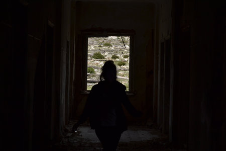A woman's silhouette in an abandoned building with an open window