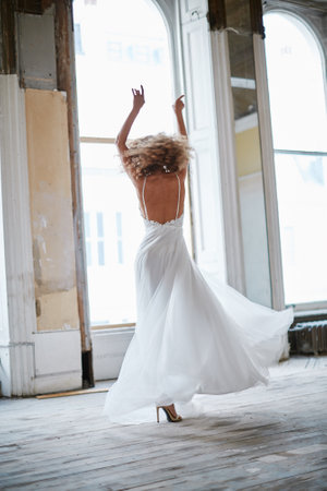A vertical shot of a blonde curly female dancing in a white dressの写真素材