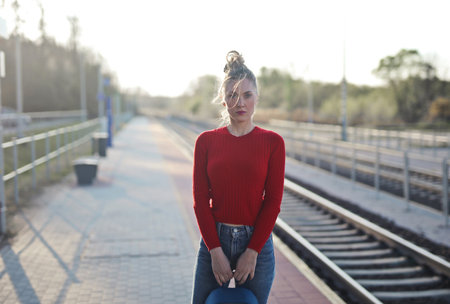 A view of a female by the railroad wearing a red blouse looking at the camera while carrying a...