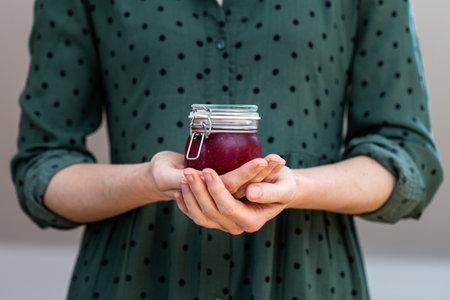 A female hands holding a homemade vegan raw raspberry jam in a glass jar
