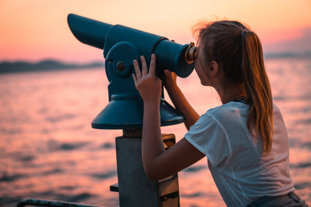 a view of a female using a telescope and looking into the sunset on the beach  from the pierの写真素材