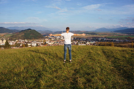 a view of a male standing on a hill with his arms open while proudly looking at his hometownの写真素材
