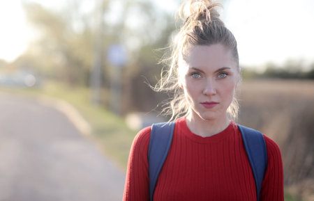 A shallow focus shot of a female by the road wearing a red blouse and seriously looking at the cameraの写真素材
