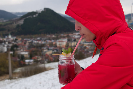 a shallow focus shot of a male drinking a pomegranate juice while looking at the city on a cold day