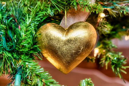 A beautiful closeup of a golden heart-shaped ornament on a Christmas tree with lightsの写真素材