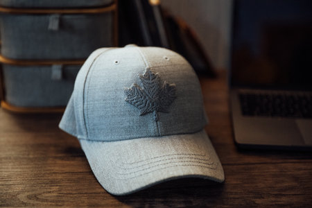 a view of a modern gray baseball cap with the design of a maple leaf on it on a wooden tableの写真素材