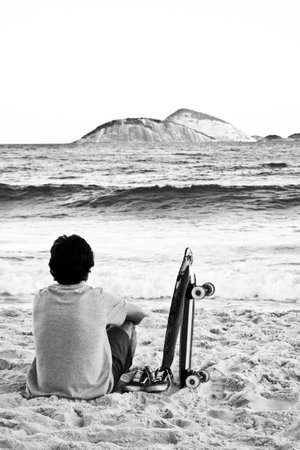 An amazing shot of a young male sitting on a beach and admiring the sea