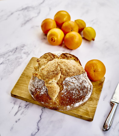A top view of a freshly baked traditional bread with oranges, lemons  and a knife