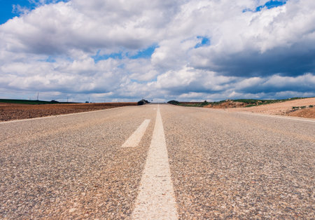 An empty road surrounded by hills under a beautiful cloudy sky