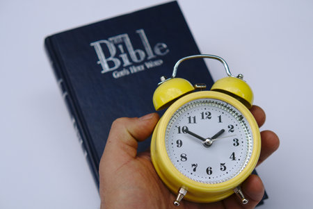 A person holding an alarm clock with the Bible in the background