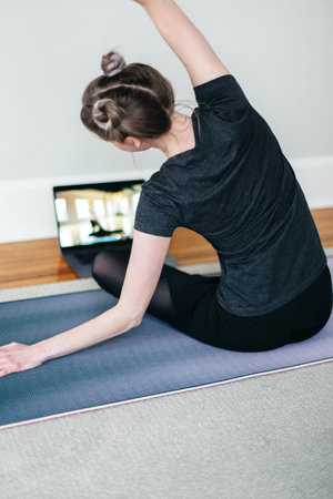 A vertical shot of a young female doing a yoga exercise and watching  yoga tutorial