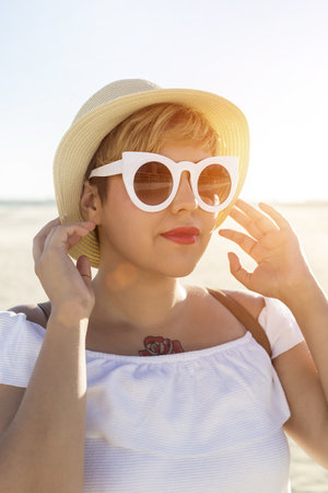A vertical shot of a female wearing white sunglasses and a hat captured on the beach