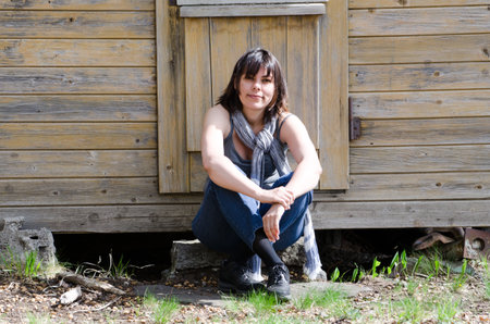 A young female sitting in front of an old wooden cabin