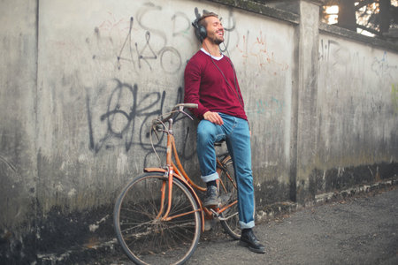 A young male listening to music and smiling standing against a wall on the streetの写真素材