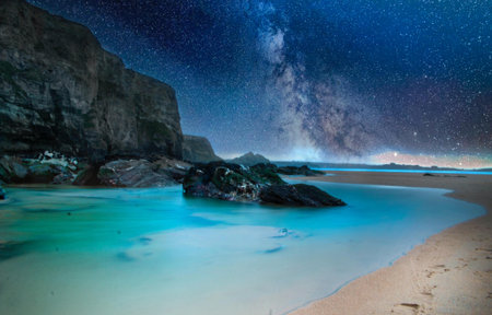 The beach surrounded by the sea and rocks under a bright starry sky at night - perfect for backgroundsの写真素材