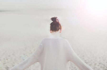A closeup shot of a young female with arms up on a sandy background