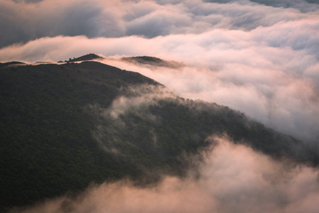 A mesmerizing shot of the clouds covering the mountains at sunsetの写真素材